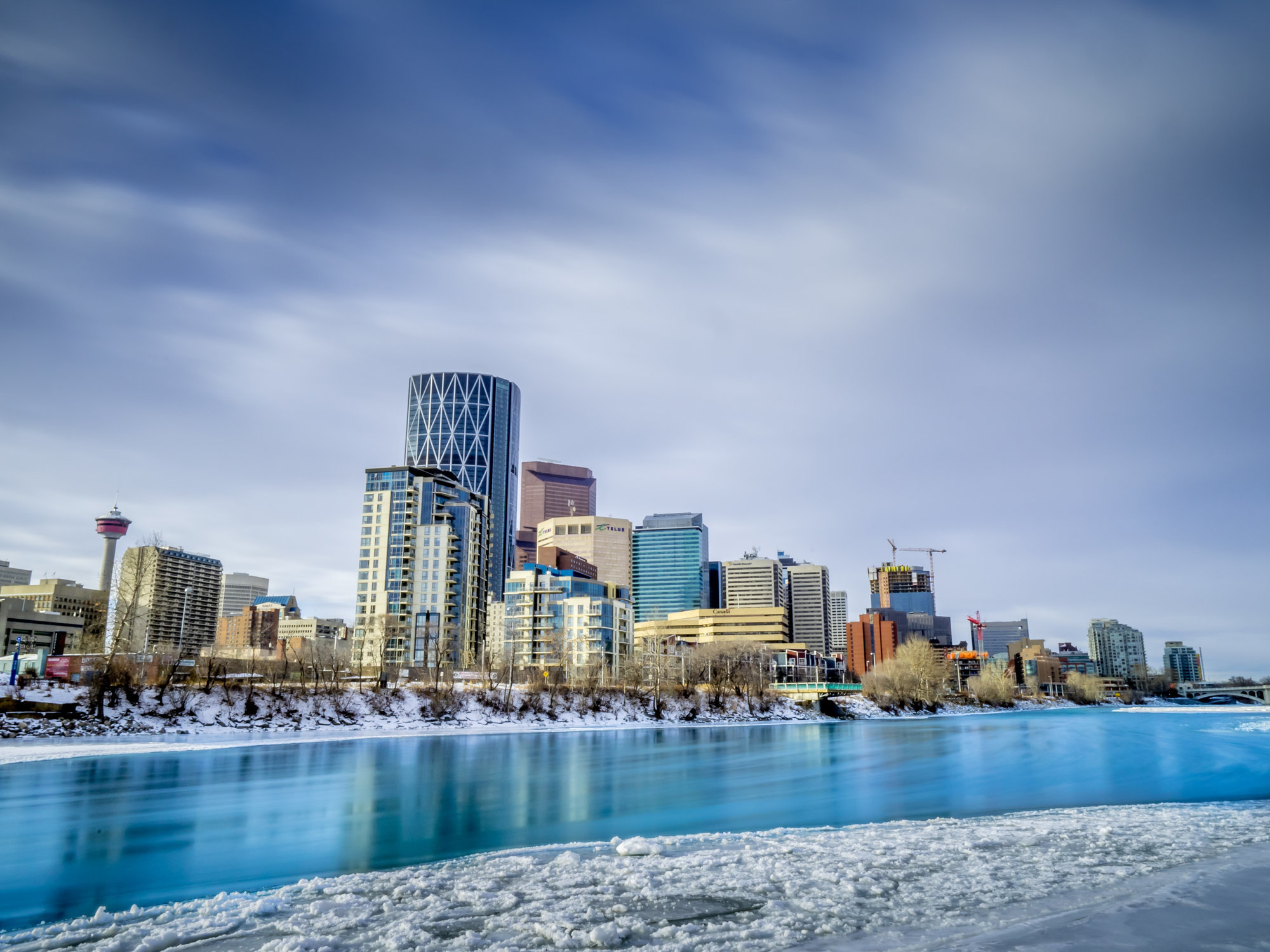 A photo of Downtown Calgary's skyline with the Bow River in the foreground that's taken from the northeast in Winter in Calgary. Real Estate Statistics, October Real Estate Stats, Homes for Sale Calgary