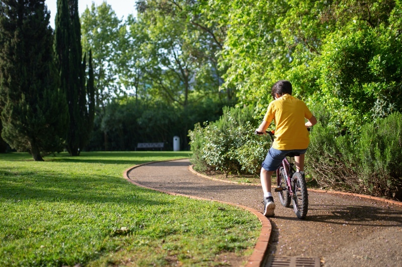 Child riding a bicycle through a park on a gravel path